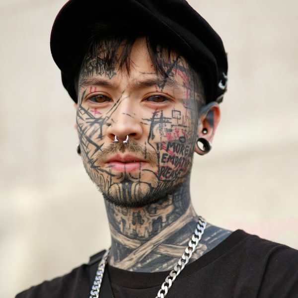 Retrato editorial de hombre con tatuajes faciales y gorra, fotografía de moda urbana por Elisabet Encina